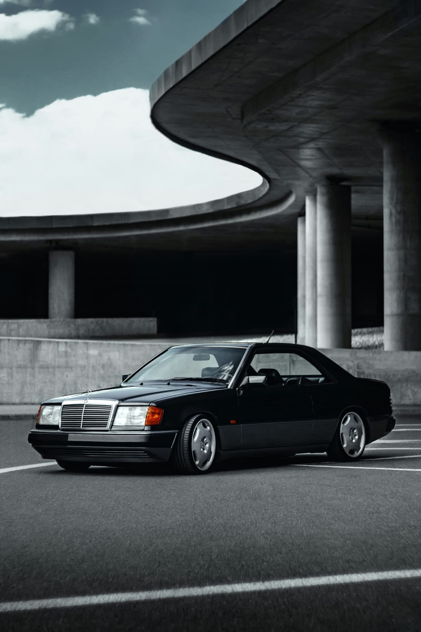 Schwarzes Mercedes-Benz E-Klasse Coupé der Baureihe C124 unter einer geschwungenen Betonbrücke